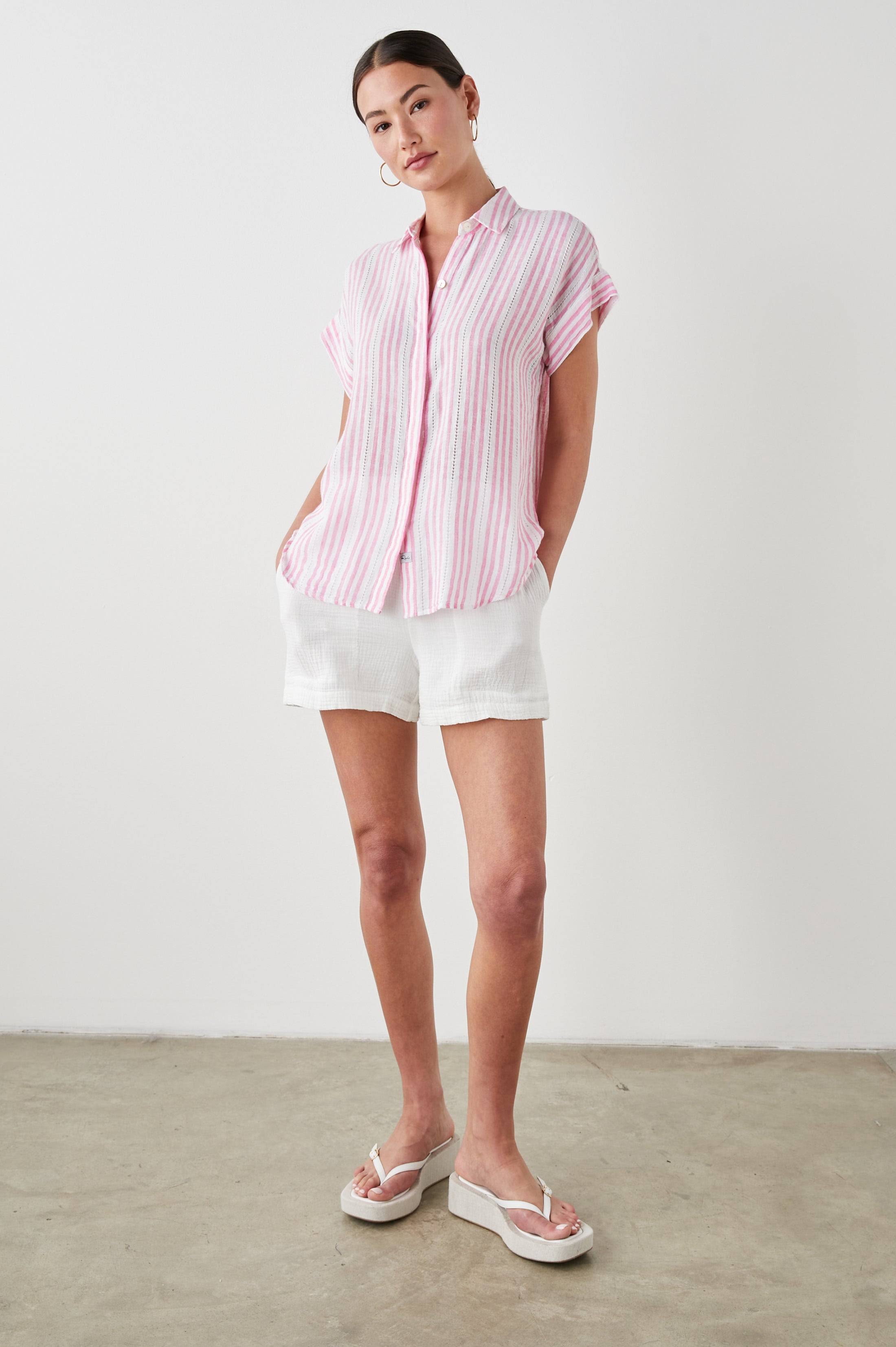Woman wearing a pink striped shirt and white shorts against a plain background