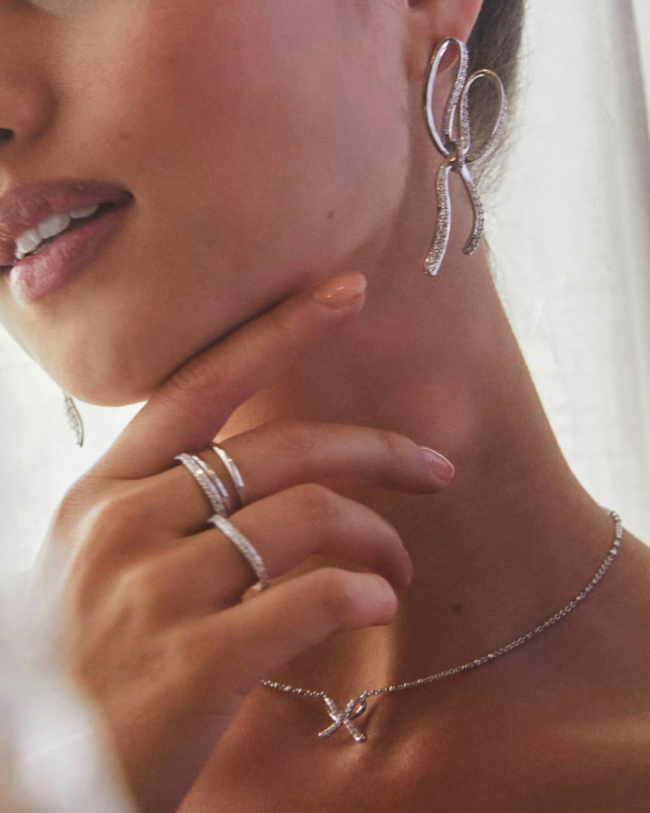 Close-up of a woman wearing silver earrings, ring, and necklace with a blurred background.