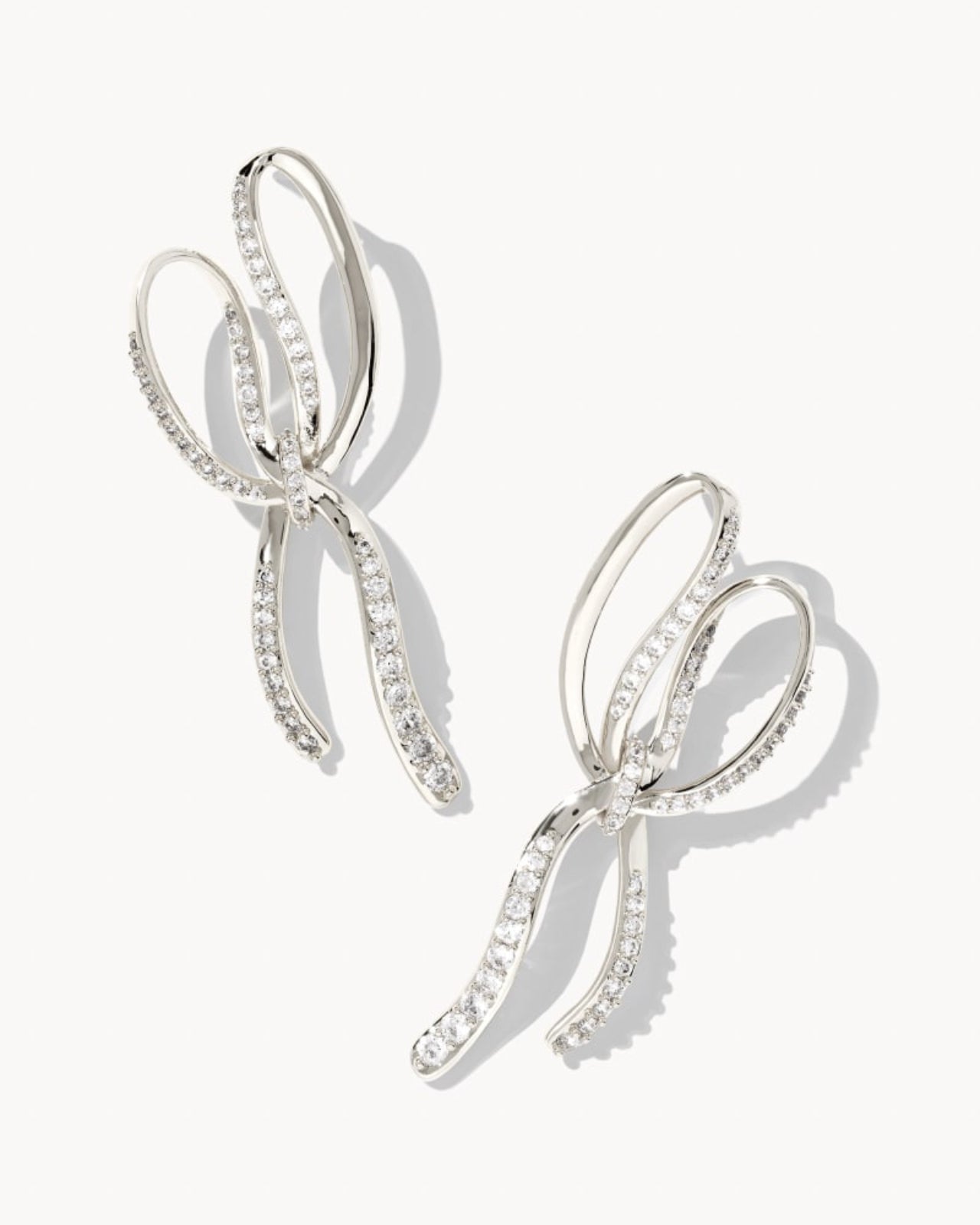 Silver bow-shaped earrings with clear stones on a white background