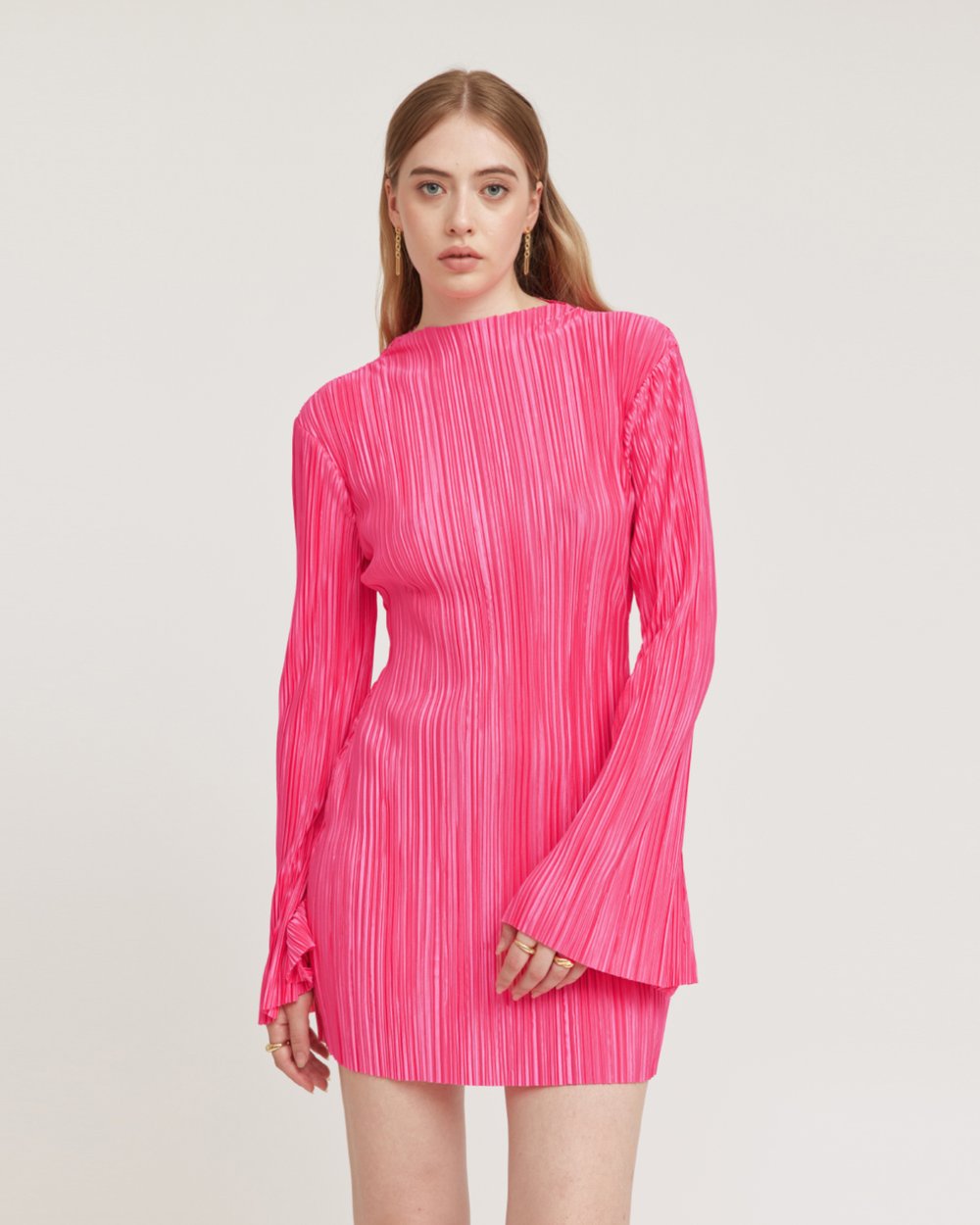 Woman wearing a bright pink pleated dress on a light gray background
