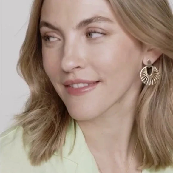 Close-up of a woman wearing gold earrings with a plain background