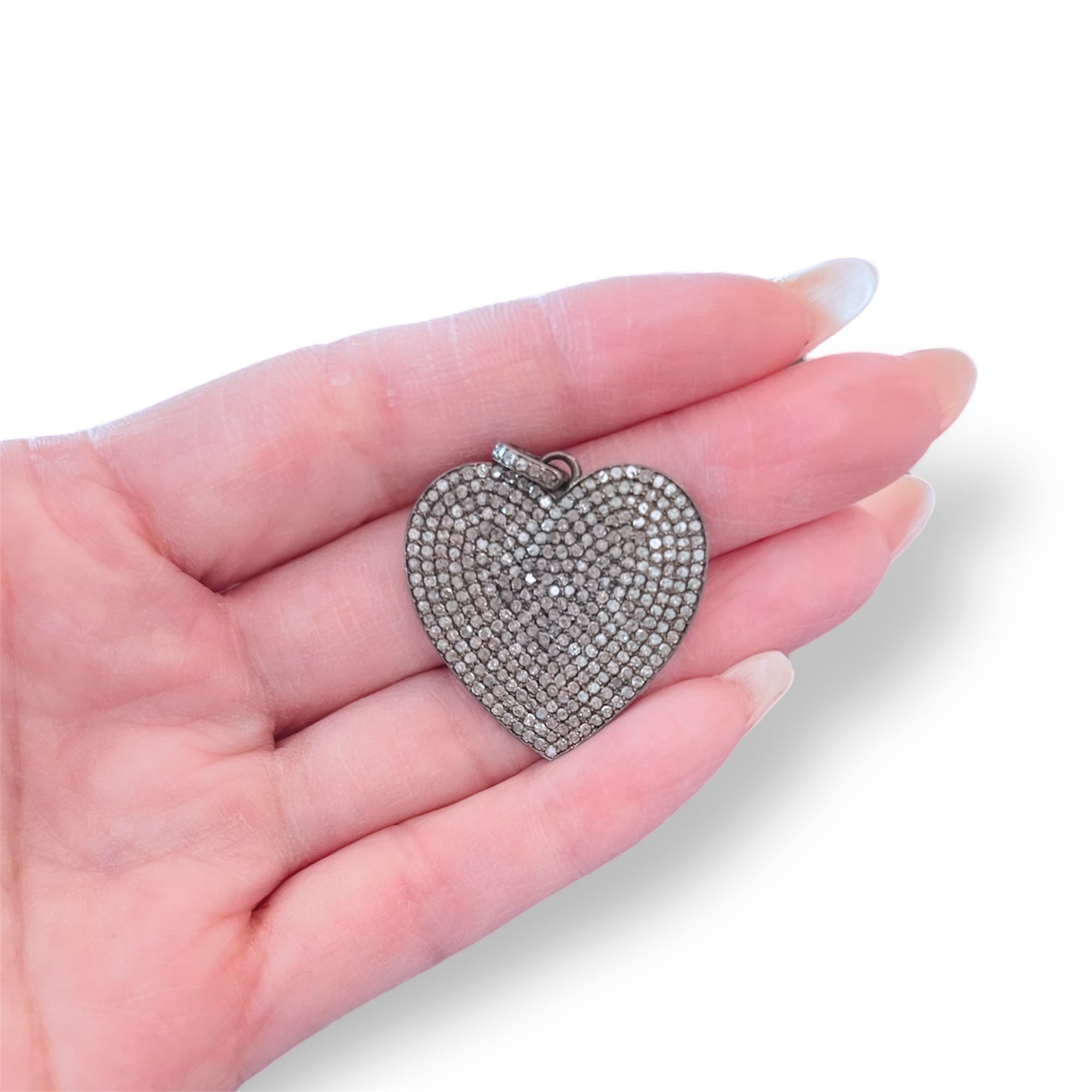 Heart-shaped silver pendant held in a hand on a white background
