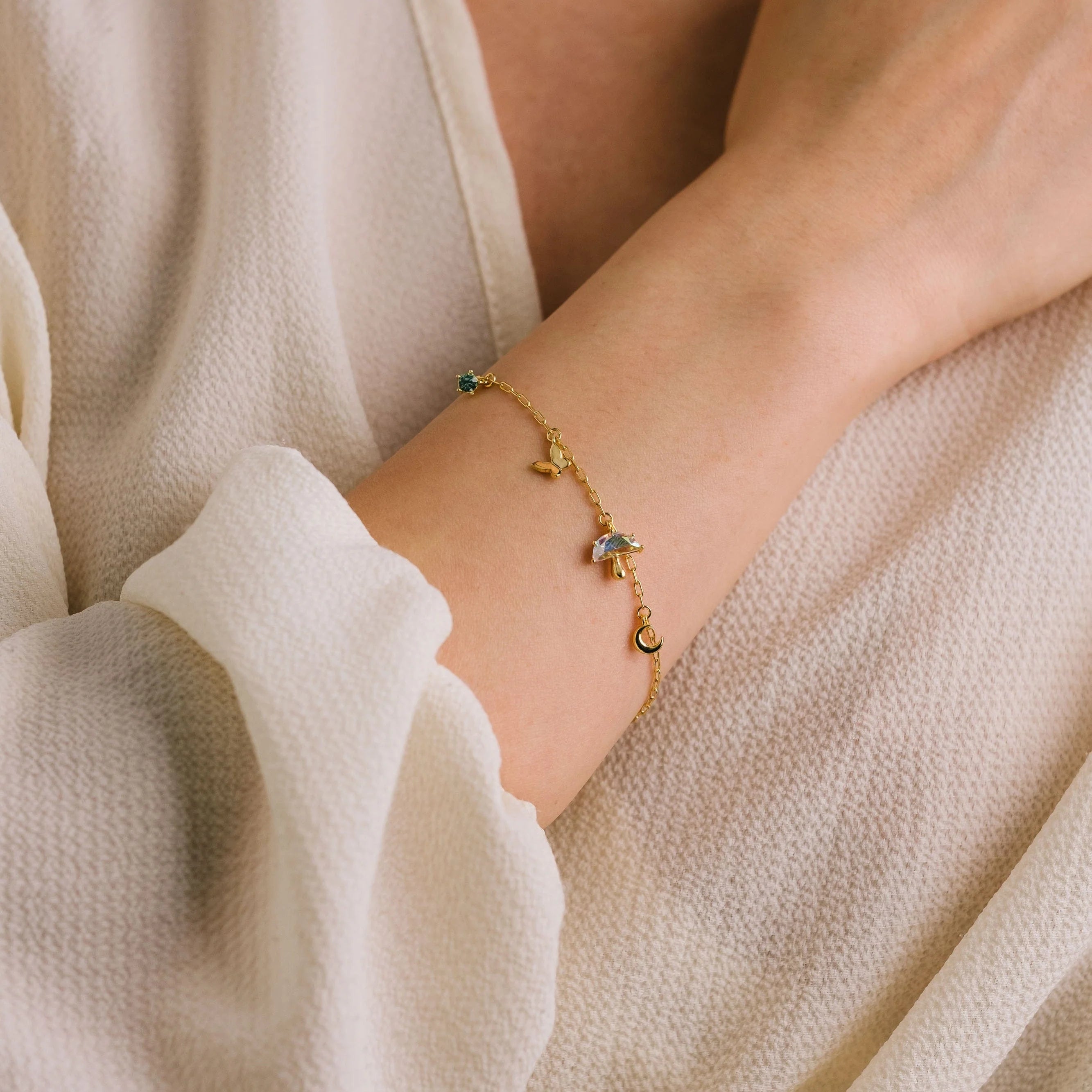 Gold bracelet with green gemstones on a wrist against a neutral background
