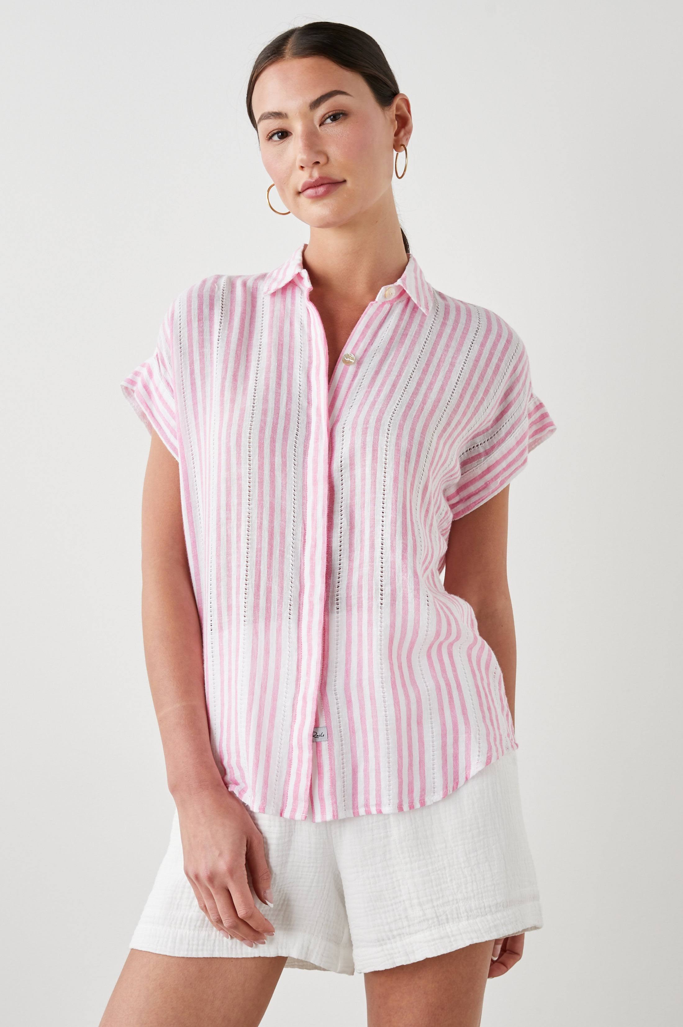 Woman wearing a pink and white striped shirt with white shorts on a light gray background