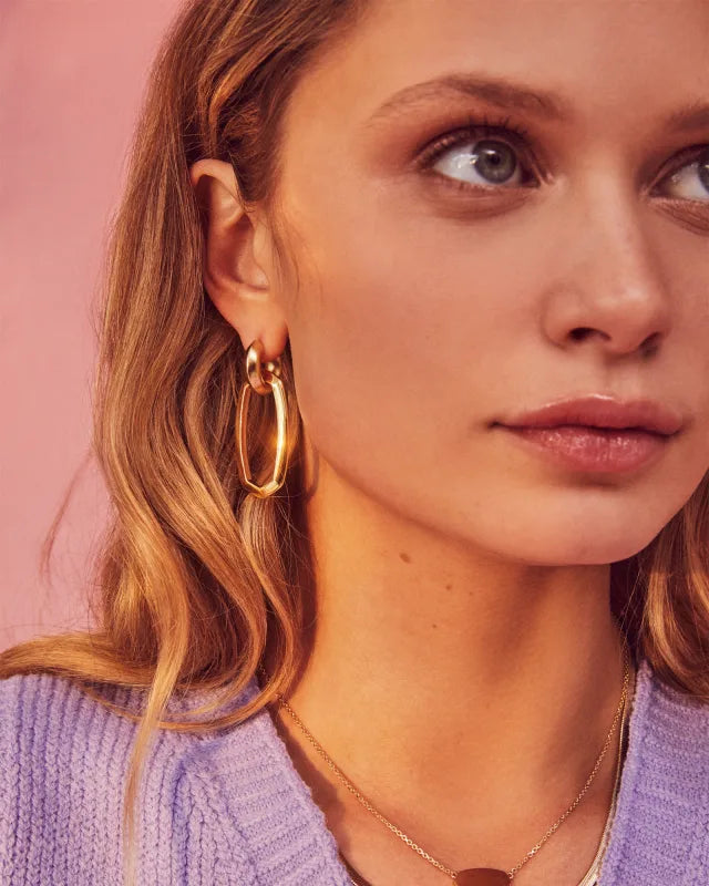 Close-up of a woman wearing gold hoop earrings with a pink background
