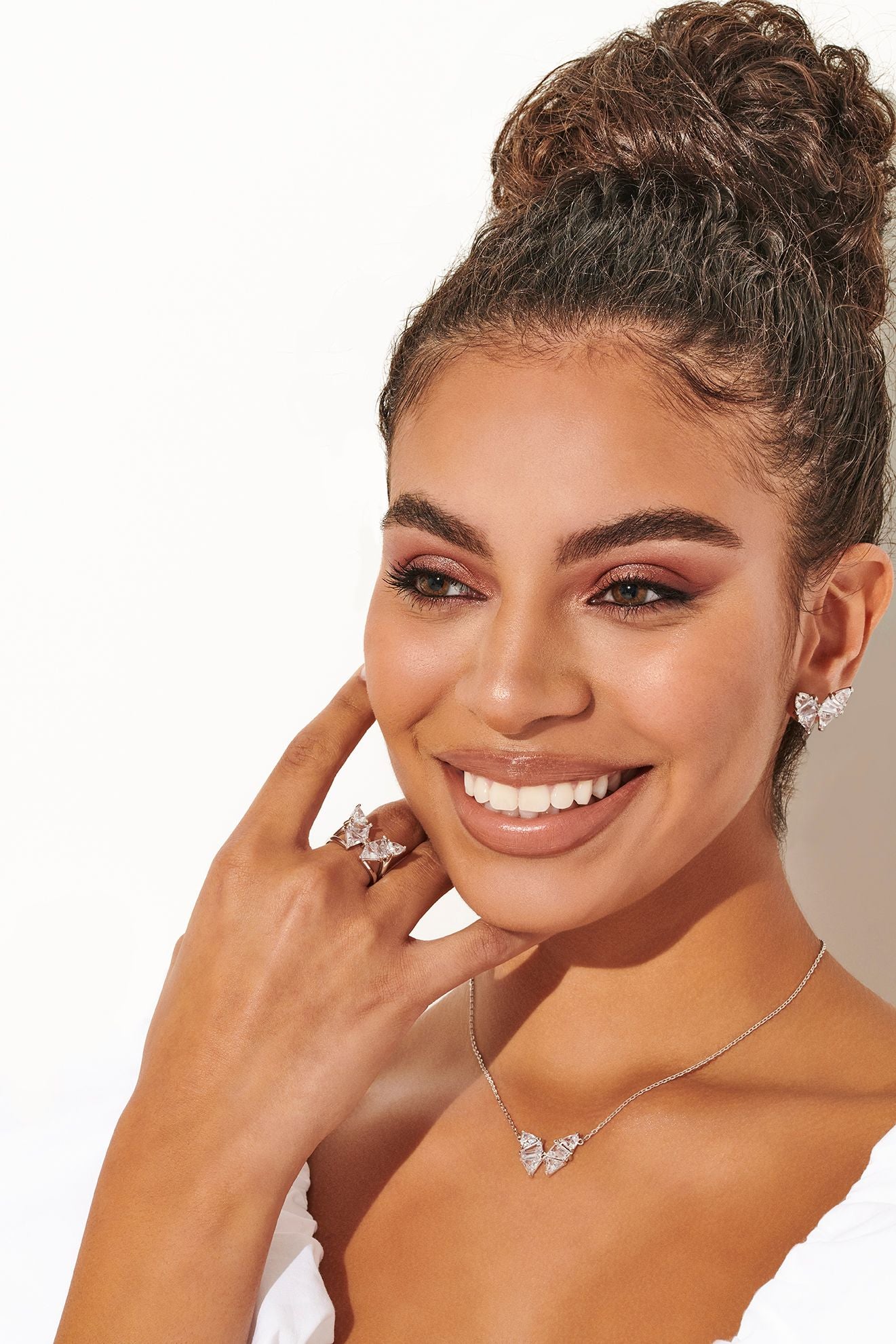 Woman wearing jewelry including a necklace, earrings, and ring on a plain background